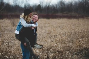 Pareja joven jugando y riendo en un campo verde, reflejando cercanía, complicidad y bienestar en la relación.
